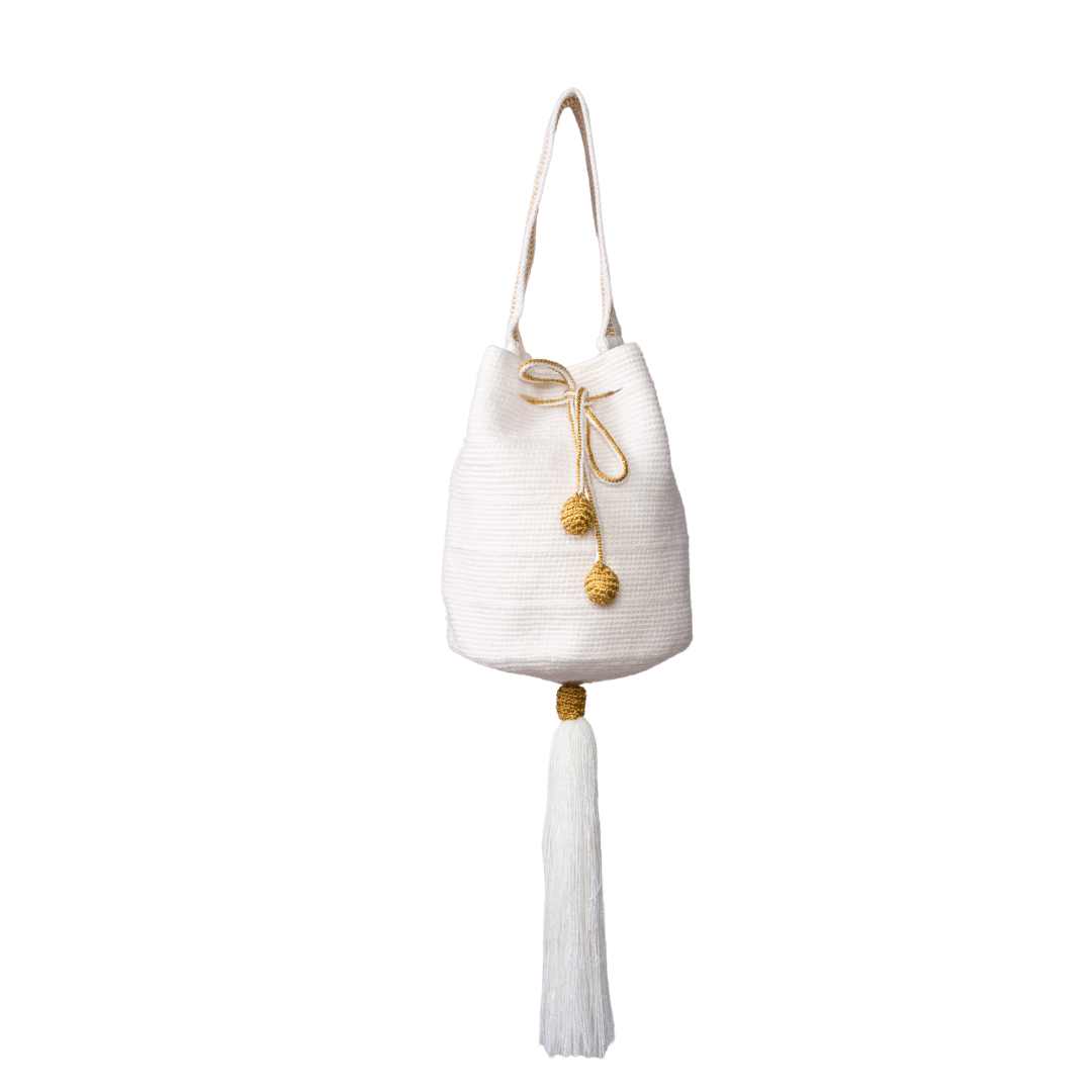 Mochila Tara Wayuu artesanal color blanco, tejida a mano con hilos de algodón y seda dorada en el norte de Colombia. Mini mochila de diseño monocromático, con textura destacada, gasa corta, cordón ajustable y bailarina colgante. Fusión de tradición y elegancia contemporánea. Mochila Wayuu, mochila de fiesta, bolso wayuu, bolso de fiesta.