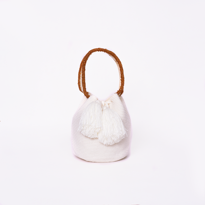 Mochila Suyan artesanal color blanco, tejida a mano por la comunidad Wayuu en el norte de Colombia. Hecha con hilos de algodón y decorada con mostacilla dorada, destaca por su diseño elegante y detalles sofisticados. Mochila de fiesta, mochila wayuu, bolso de fiesta.