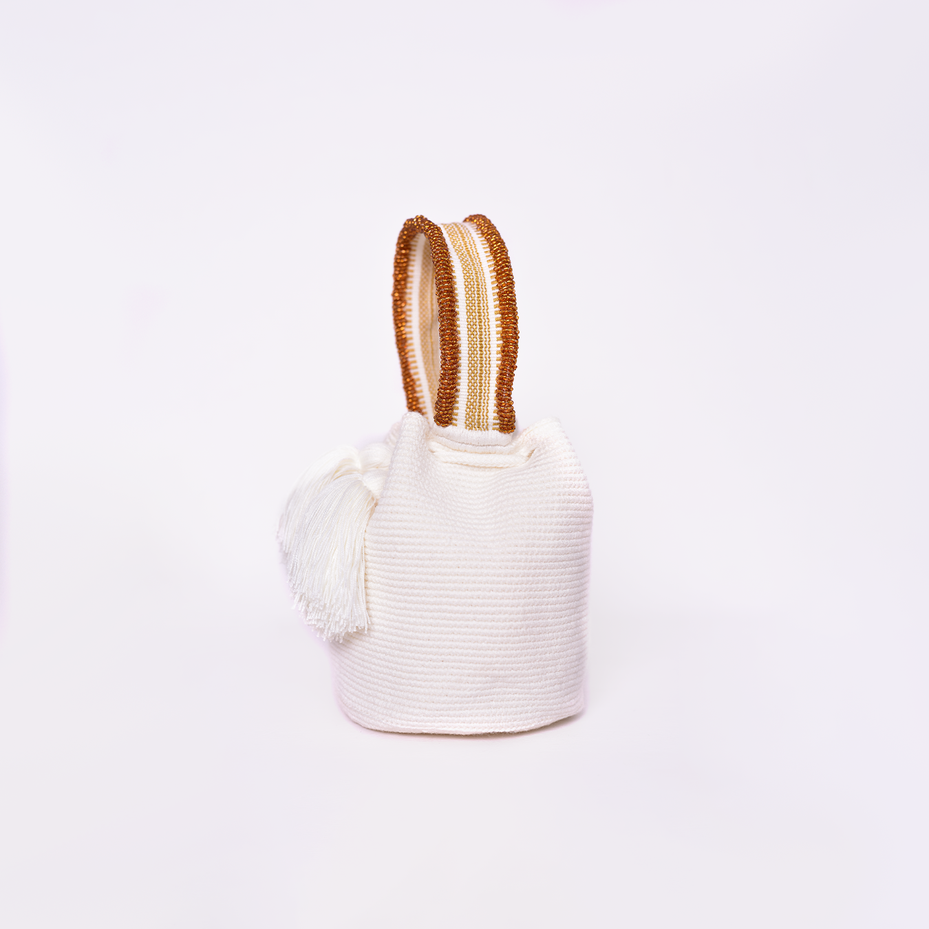 Mochila Suyan artesanal color blanco, tejida a mano por la comunidad Wayuu en el norte de Colombia. Hecha con hilos de algodón y decorada con mostacilla dorada, destaca por su diseño elegante y detalles sofisticados. Mochila de fiesta, mochila wayuu, bolso de fiesta.