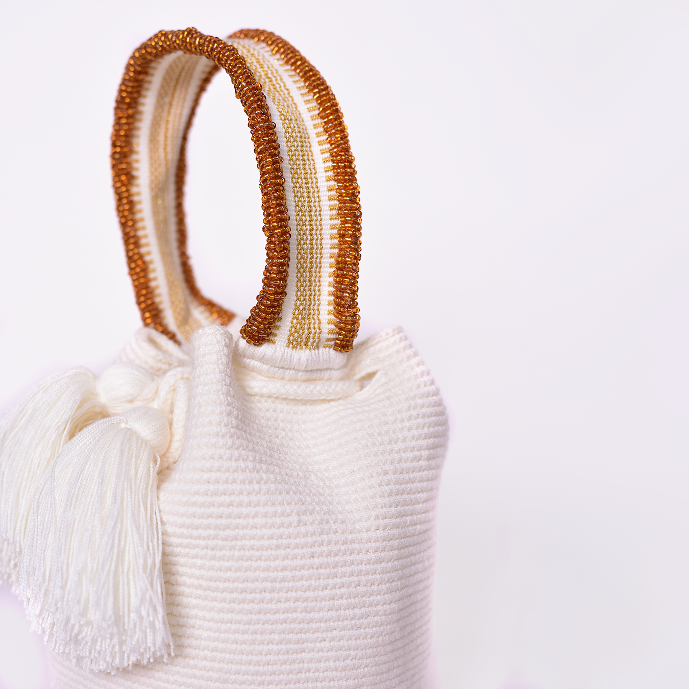 Mochila Suyan artesanal color blanco, tejida a mano por la comunidad Wayuu en el norte de Colombia. Hecha con hilos de algodón y decorada con mostacilla dorada, destaca por su diseño elegante y detalles sofisticados. Mochila de fiesta, mochila wayuu, bolso de fiesta.