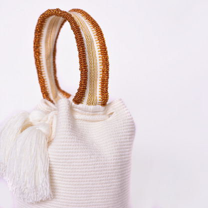 Mochila Suyan artesanal color blanco, tejida a mano por la comunidad Wayuu en el norte de Colombia. Hecha con hilos de algodón y decorada con mostacilla dorada, destaca por su diseño elegante y detalles sofisticados. Mochila de fiesta, mochila wayuu, bolso de fiesta.