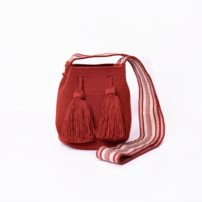 Mochila Amaranta Wayuu, elaborada a mano por artesanas de la comunidad Wayuu en el norte de La Guajira, Colombia. Esta mochila única destaca por su diseño auténtico y práctico, tejida 100% a mano con dedicación. Cuenta con un asa larga para llevarla cómodamente al hombro o cruzada, y dos bailarinas ajustables que no solo aportan un toque decorativo, sino que también garantizan un cierre seguro para proteger tus pertenencias. Color terracota.