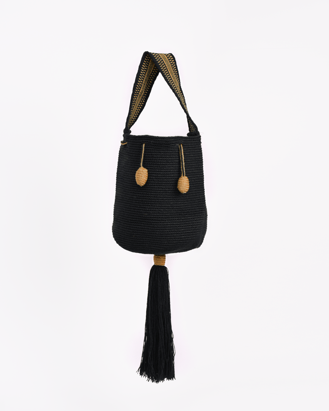 Mochila Tara Wayuu artesanal color negro, tejida a mano con hilos de algodón y seda dorada en el norte de Colombia. Mini mochila de diseño monocromático, con textura destacada, gasa corta, cordón ajustable y bailarina colgante. Fusión de tradición y elegancia contemporánea. Mochila Wayuu, mochila de fiesta, bolso wayuu, bolso de fiesta.