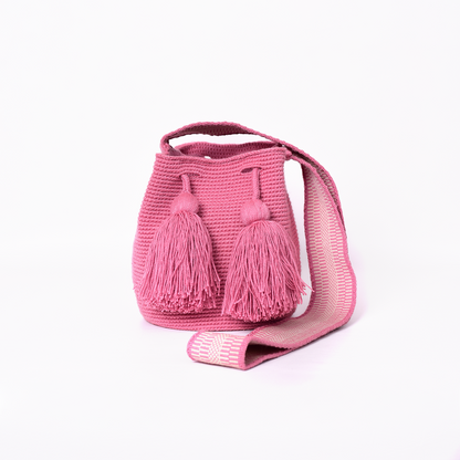Mochila Amaranta Wayuu, elaborada a mano por artesanas de la comunidad Wayuu en el norte de La Guajira, Colombia. Esta mochila única destaca por su diseño auténtico y práctico, tejida 100% a mano con dedicación. Cuenta con un asa larga para llevarla cómodamente al hombro o cruzada, y dos bailarinas ajustables que no solo aportan un toque decorativo, sino que también garantizan un cierre seguro para proteger tus pertenencias. Color rosado.