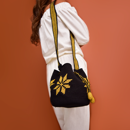Mochila Marlen, mochila artesanal hecha a mano por artesanas de la comunidad Wayuu en el norte de Colombia. Tejida con hilos de algodón y seda dorada. Su diseño de flores tejidas aporta elegancia atemporal, mientras que su gasa larga y cordón ajustable. Mochila wayuu, mochila colombiana, bolso colombiano, bolso artesanal, mochila artesanal.