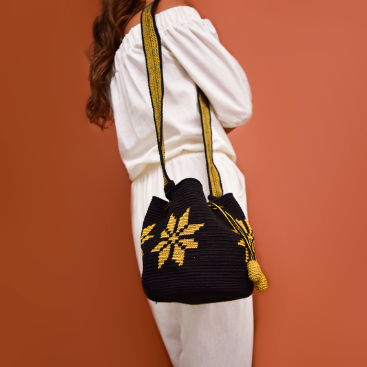 Mochila Marlen, mochila artesanal hecha a mano por artesanas de la comunidad Wayuu en el norte de Colombia. Tejida con hilos de algodón y seda dorada. Su diseño de flores tejidas aporta elegancia atemporal, mientras que su gasa larga y cordón ajustable. Mochila wayuu, mochila colombiana, bolso colombiano, bolso artesanal, mochila artesanal.