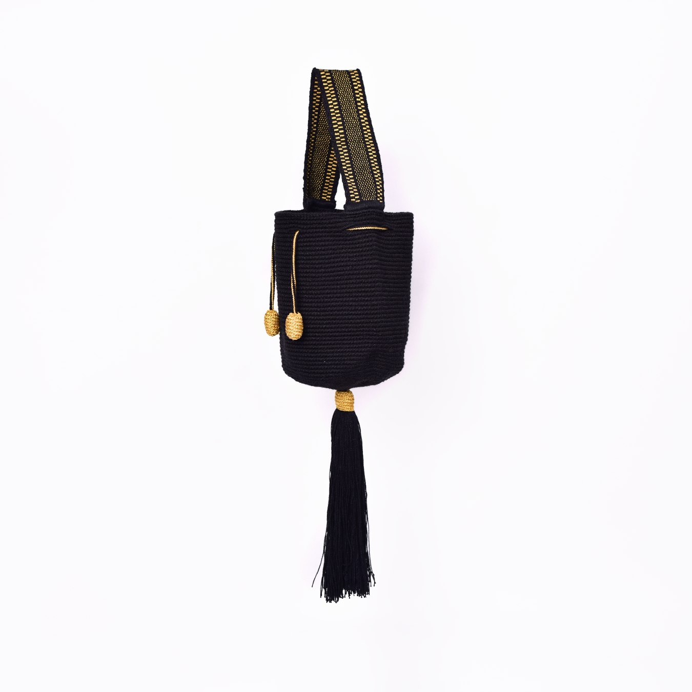 Mochila Tara Wayuu artesanal color negro, tejida a mano con hilos de algodón y seda dorada en el norte de Colombia. Mini mochila de diseño monocromático, con textura destacada, gasa corta, cordón ajustable y bailarina colgante. Fusión de tradición y elegancia contemporánea. Mochila Wayuu, mochila de fiesta, bolso wayuu, bolso de fiesta.