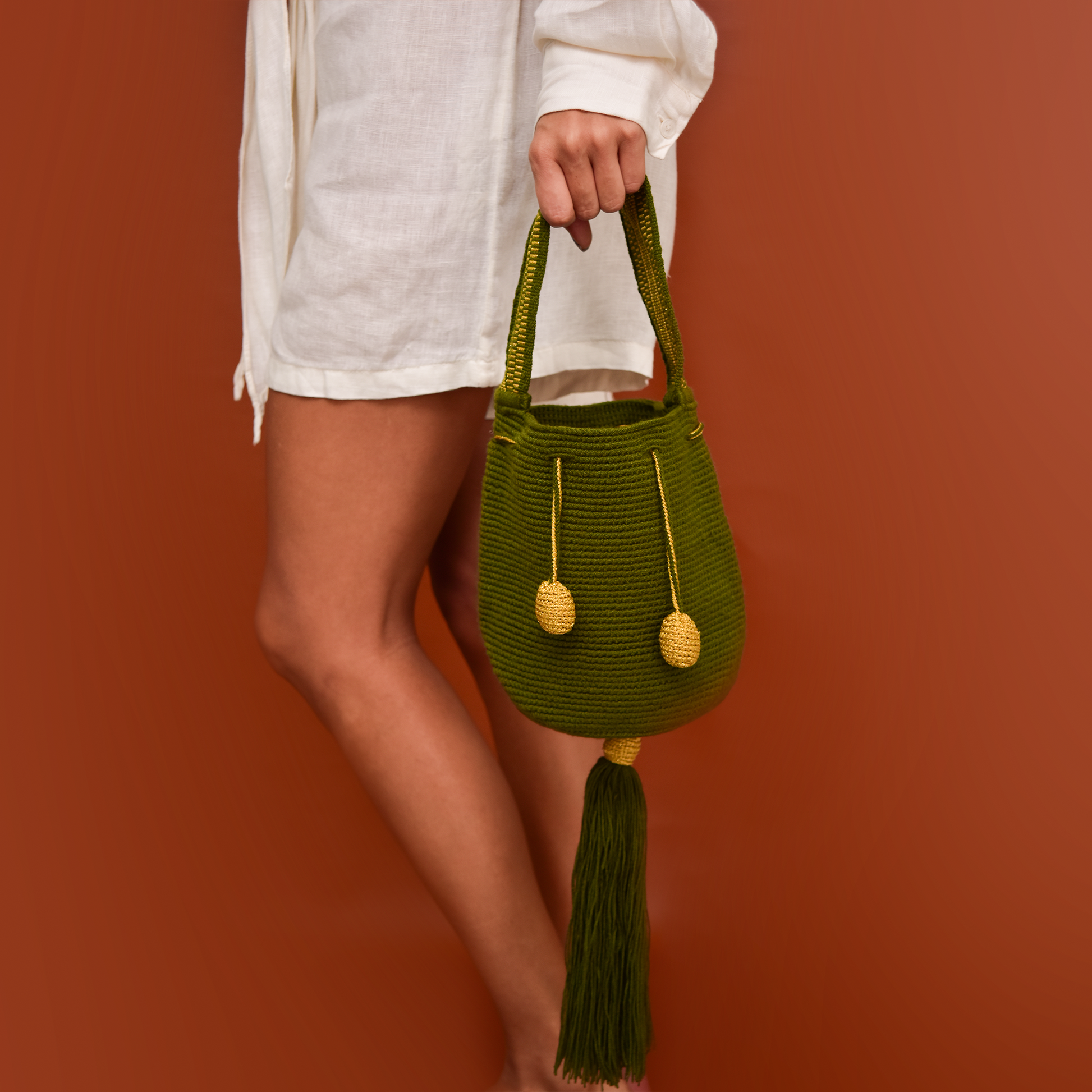 Mochila Tara Wayuu artesanal color verde militar, tejida a mano con hilos de algodón y seda dorada en el norte de Colombia. Mini mochila de diseño monocromático, con textura destacada, gasa corta, cordón ajustable y bailarina colgante. Fusión de tradición y elegancia contemporánea. Mochila Wayuu, mochila de fiesta, bolso wayuu, bolso de fiesta.