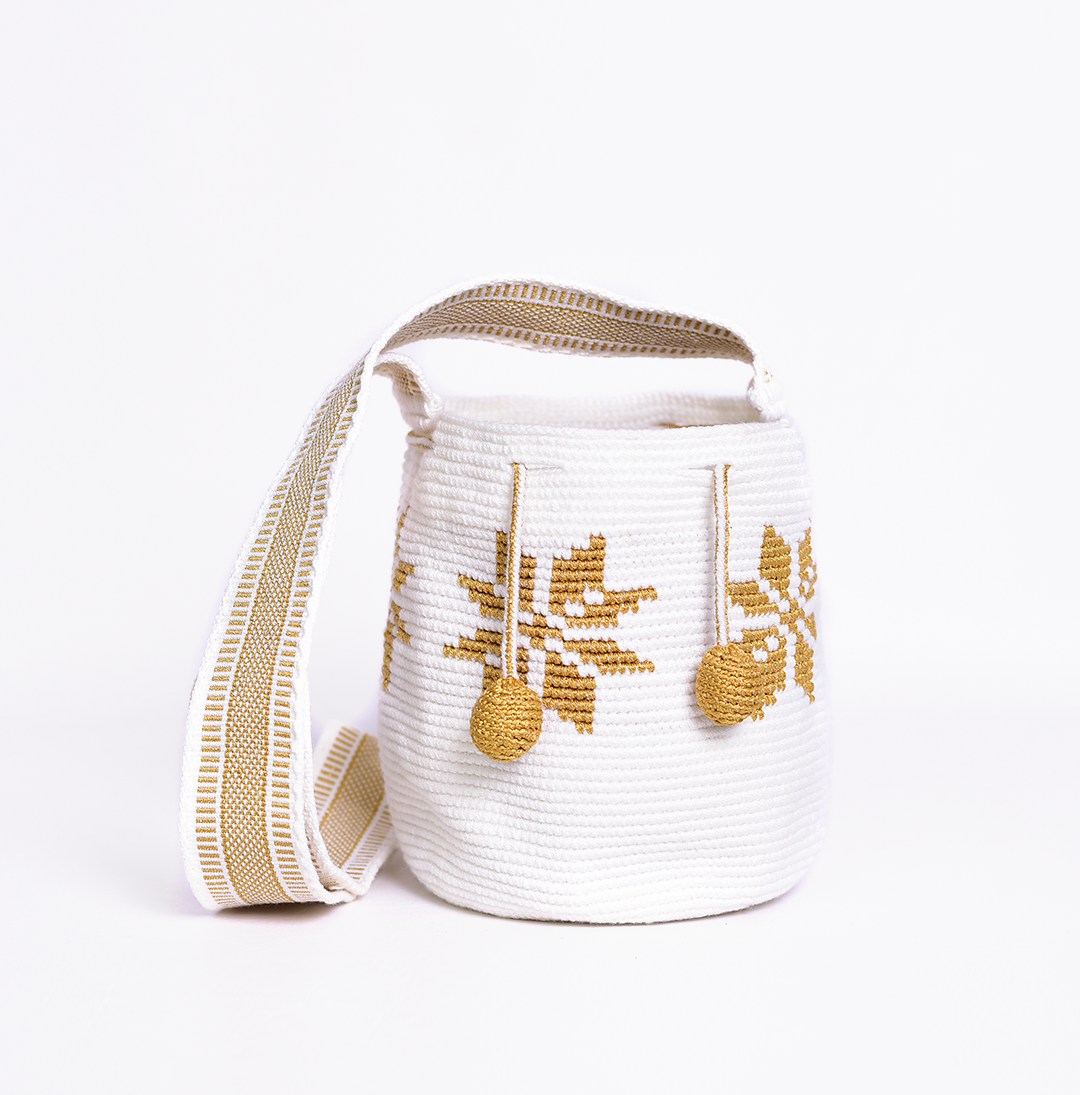 Mochila Marlen, mochila artesanal hecha a mano por artesanas de la comunidad Wayuu en el norte de Colombia. Tejida con hilos de algodón y seda dorada. Su diseño de flores tejidas aporta elegancia atemporal, mientras que su gasa larga y cordón ajustable. Mochila wayuu, mochila colombiana, bolso colombiano, bolso artesanal, mochila artesanal, color blanco.