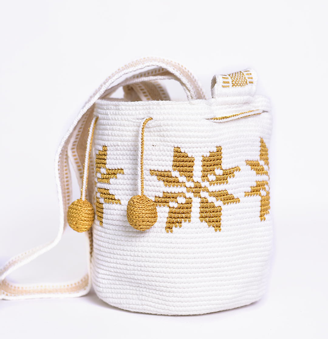 Mochila Marlen, mochila artesanal hecha a mano por artesanas de la comunidad Wayuu en el norte de Colombia. Tejida con hilos de algodón y seda dorada. Su diseño de flores tejidas aporta elegancia atemporal, mientras que su gasa larga y cordón ajustable. Mochila wayuu, mochila colombiana, bolso colombiano, bolso artesanal, mochila artesanal.