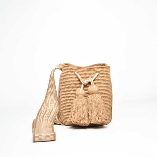 Mochila Amaranta Wayuu, elaborada a mano por artesanas de la comunidad Wayuu en el norte de La Guajira, Colombia. Esta mochila única destaca por su diseño auténtico y práctico, tejida 100% a mano con dedicación. Cuenta con un asa larga para llevarla cómodamente al hombro o cruzada, y dos bailarinas ajustables que no solo aportan un toque decorativo, sino que también garantizan un cierre seguro para proteger tus pertenencias. Color camel.