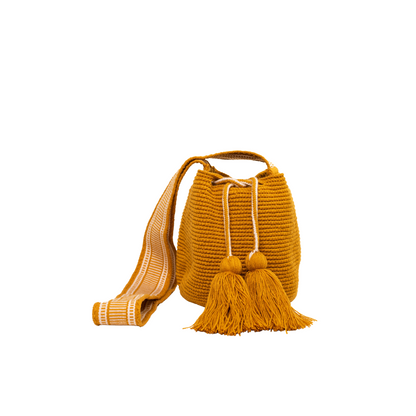 Mochila Amaranta Wayuu, elaborada a mano por artesanas de la comunidad Wayuu en el norte de La Guajira, Colombia. Esta mochila única destaca por su diseño auténtico y práctico, tejida 100% a mano con dedicación. Cuenta con un asa larga para llevarla cómodamente al hombro o cruzada, y dos bailarinas ajustables que no solo aportan un toque decorativo, sino que también garantizan un cierre seguro para proteger tus pertenencias. Color mostaza.